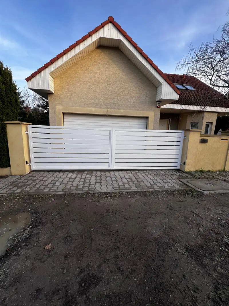 Biała brama i ogrodzenie przy domu z garażem