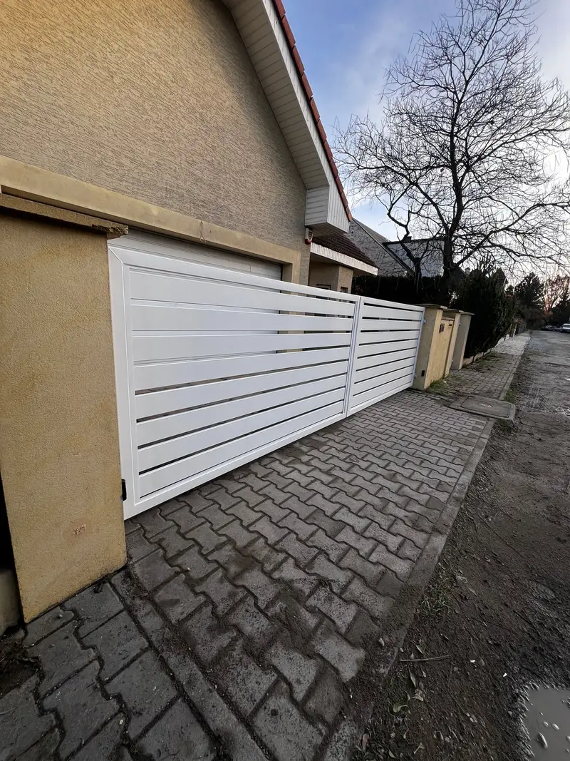 Białe ogrodzenie z szerokich profili wzdłuż podjazdu