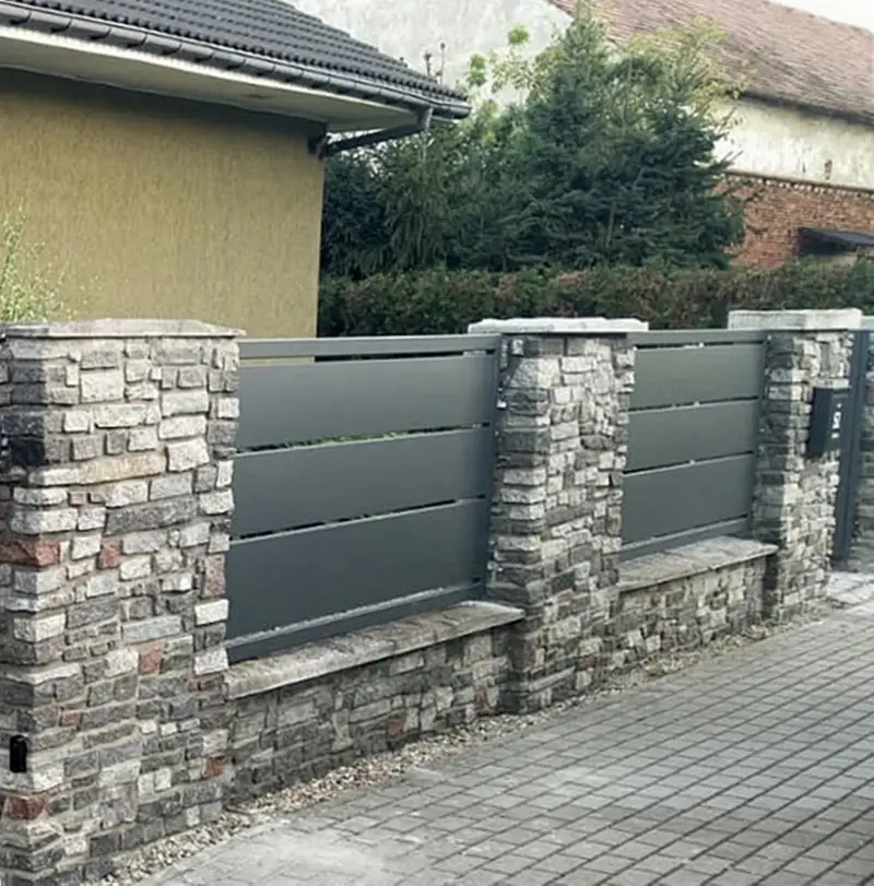Ogrodzenie z szerokich profili między słupkami z kamienia dekoracyjnego